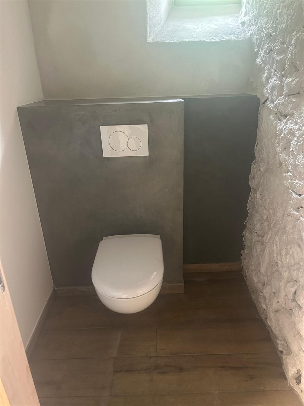 WC en béton ciré gris contrastant avec un mur en pierre apparente